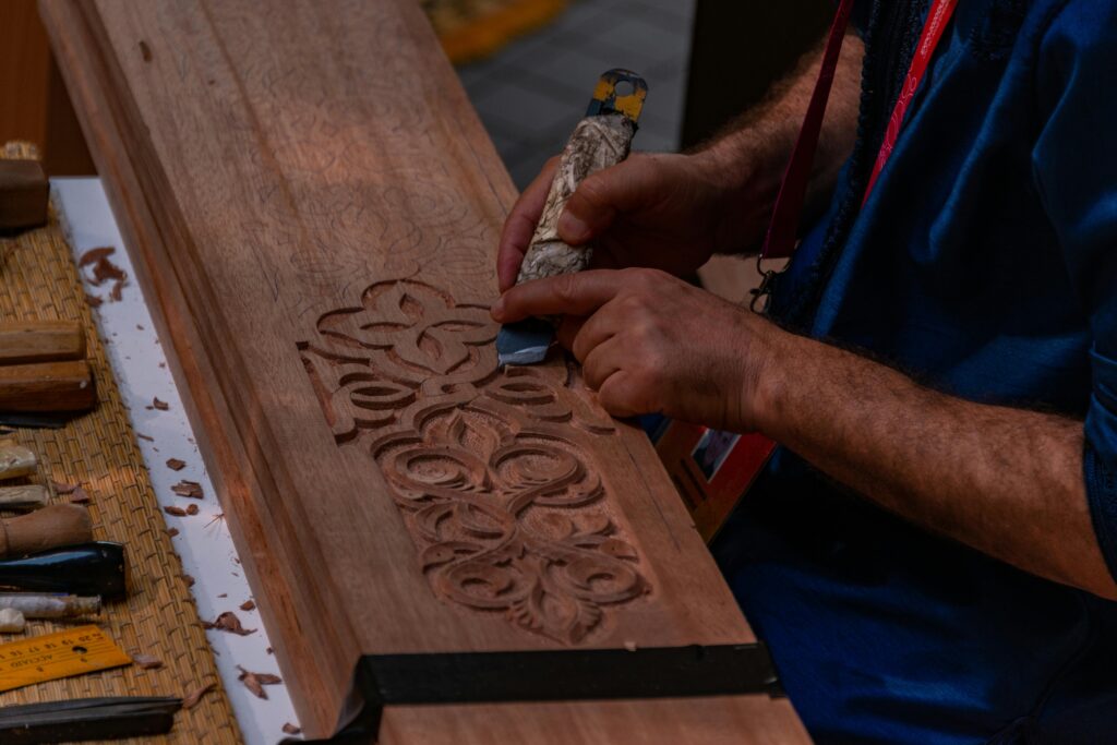 Close-up of hands intricately carving a wooden panel, showcasing craftsmanship and woodworking skill.